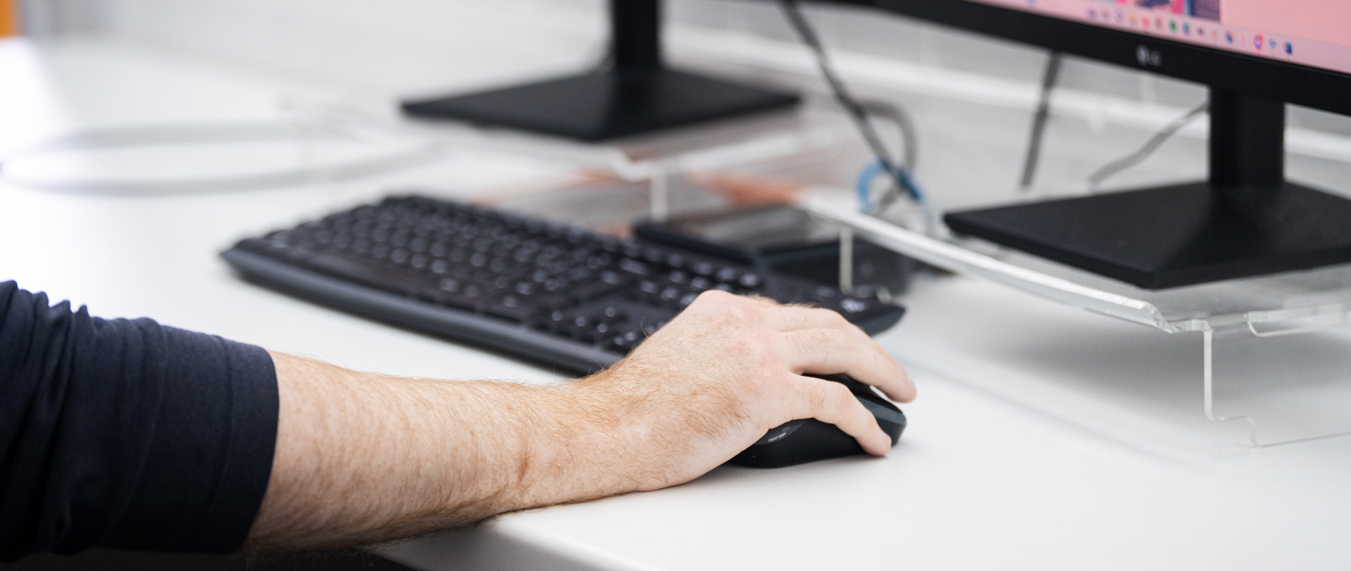 A man's hand using a mouse connected to a desktop computer