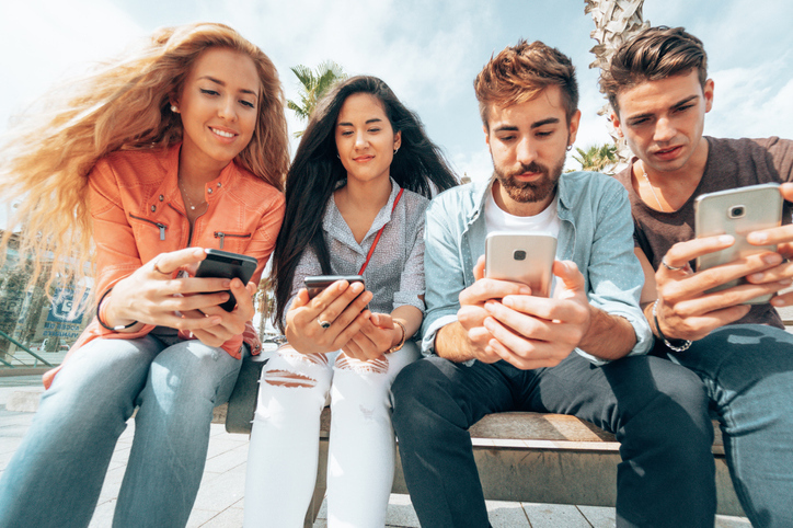 A group of 4 teenagers sat down browsing through their phone.